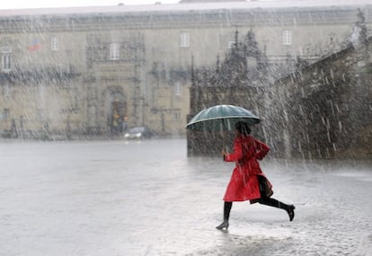 Una mujer cruza, bajo un intenso aguacero, la plaza del Obradoiro de Santiago de Compostela.