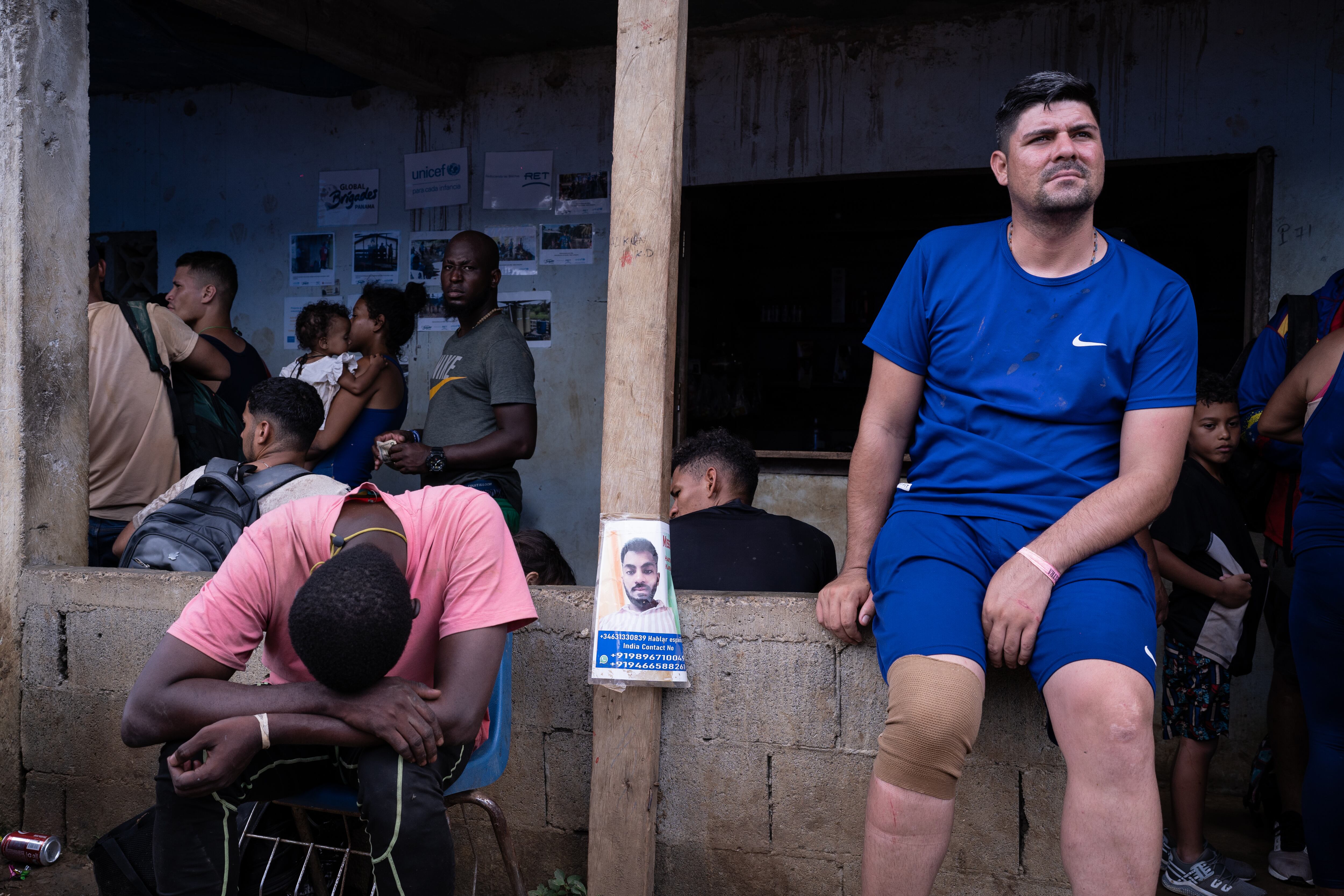 Migrantes descansan en Bajo Chiquito después de salir de la selva al lado de un cartel con la imagen de un hombre desaparecido.’Missing. Indian Contact. Hablar español’.