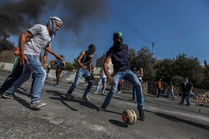 Unos jóvenes palestinos encapuchados juegan al fútbol en un descanso de los enfrentamientos con los soldados israelíes en la entrada principal de la ciudad de Belén, en Cisjordania.