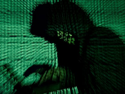 Un hombre sostiene una ordenador mientras se proyecta un código cibernético sobre él.