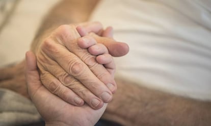 Un cuidador da la mano a un hombre en situación de dependencia. 