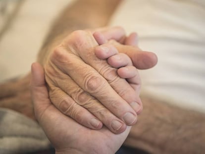 Un cuidador da la mano a un hombre en situación de dependencia. 