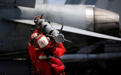 Un miembro del personal de la armada estadounidense transporta un misil para armar a un caza de combate F18 en la cubierta del portaviones USS Carl Vinson.