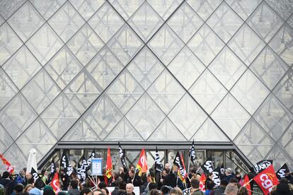 Algunos empleados sujetan pancartas y banderas de sindicatos mientras bloquean la entrada Louvre para denunciar la controvertida reforma de las pensiones del Gobierno, este lunes en París.