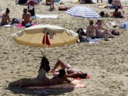 Unos bañistas toman el sol y se protegen bajo las sombrillas en la playa de la Barceloneta. EFE/Archivo