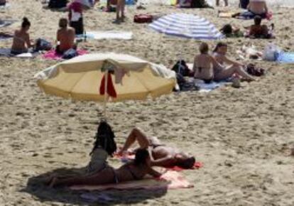Unos bañistas toman el sol y se protegen bajo las sombrillas en la playa de la Barceloneta. EFE/Archivo