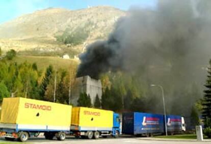 Varios camiones esperan en la entrada del túnel de Gotardo, donde se produjo un accidente. Detrás, una columna de humo sale por un respiradero.