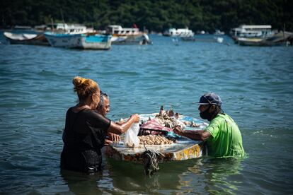 Un vendedor ofrece sus productos dentro del agua en la playa de Caleta.