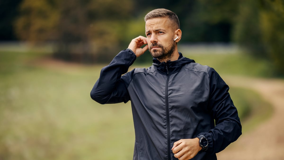 Un hombre ajustando sus auriculares mientras se prepara para el entrenamiento al aire libre.