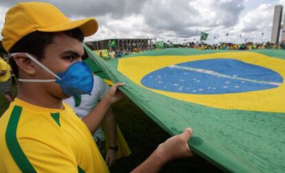 Un joven con mascarilla sujeta la bandera de Brasil en la manifestación.