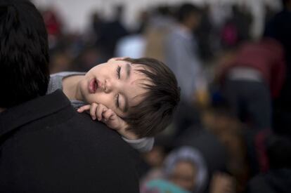 Un hombre sostiene a un niño dormido mientras espera junto a otros migrantes y refugiados a coger un tren que le lleve a Serbia desde la frontera greco-macedonia en la localidad de Gevgelija el pasado 28 de octubre.