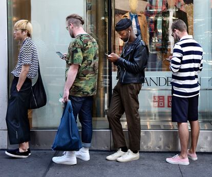 Varias personas usan sus teléfonos móviles mientras hacen cola frente a una tienda en Nueva York.