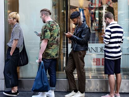 Varias personas usan sus teléfonos móviles mientras hacen cola frente a una tienda en Nueva York.