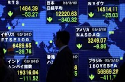 Peatones caminan junto a una pantalla informativa que muestra el índice de la bolsa en Tokio (Japón).
