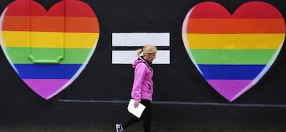 Una mujer camina junto a una pintada de dos corazones con los colores del arco&iacute;ris en Dubl&iacute;n.