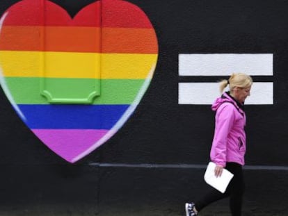 Una mujer camina junto a una pintada de dos corazones con los colores del arco&iacute;ris en Dubl&iacute;n.