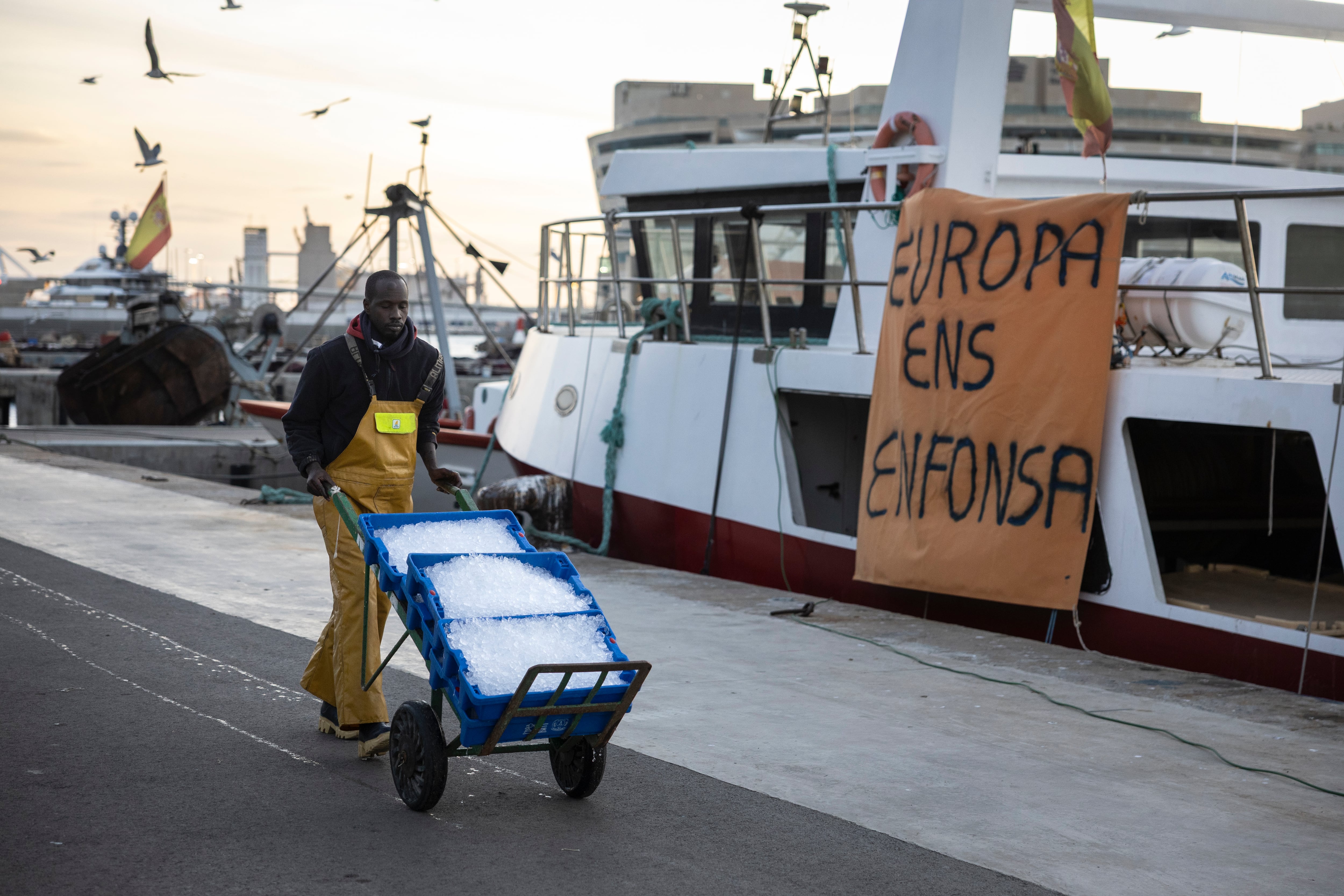 Un pescador camina frente a un cartel de protesta colgado en un pesquero amarrado en el muelle del Port Vell de Barcelona.