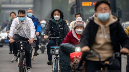 Viajeros en bicicleta usan mascarilla por una calle en el distrito comercial central de Pekín, el 20 de octubre de 2022.