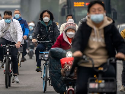 Viajeros en bicicleta usan mascarilla por una calle en el distrito comercial central de Pekín, el 20 de octubre de 2022.