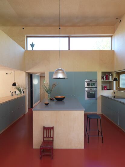 La cocina es un diseño de Jeppe Utzon en el que su madre impuso el color: el verde pálido de la hierba de centeno que crece junto al mar. El suelo, rojo anaranjado, también fue elegido por la dueña. Sobre la zona de trabajo, cuencos metálicos de la mítica colección Krenit, del diseñador danés Herbert Krenchel. Los taburetes negros son de la empresa Hay Copenhagen, la silla roja infantil lleva décadas en la familia, las lámparas pequeñas negras son de la casa italiana Ilva y las grandes —de aluminio y aspecto industrial— las produce la empresa italiana B&W.