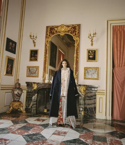 En el Palacio Real de La Granja de San Ildefonso, África lleva un abrigo en paño azul sobre caftán de lino floral, camisa inspirada en la ropa interior del siglo XVII con cuello en croché y pantalón vaquero estampado, todo de Palomo Spain. El lino se ha elaborado en colaboración con The Rosa Bernal Collection, especializada en el desarrollo de tejidos siguiendo técnicas ancestrales.