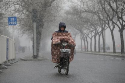 Una mujer monta en una bicicleta eléctrica durante una nevada en Pekín (China).