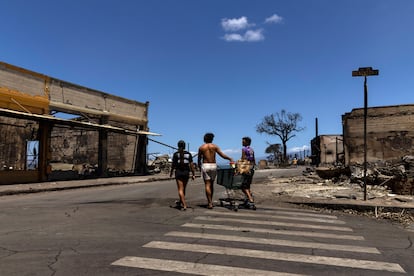 Residents push a kart amid the ruins left by a wildfire that swept through the city up to the shore and port in Lahaina.