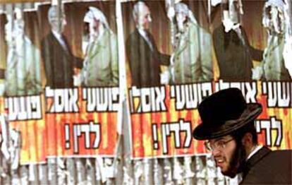 Un judío ortodoxo pasa por un calle de Jerusalén ante un cartel en el que se califica a Peres y Arafat de criminales.