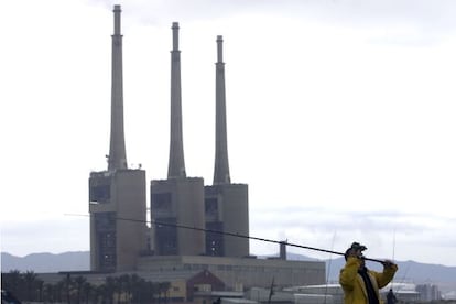 Un hombre pesca en el río Besòs con la silueta de las tres chimeneas al fondo.