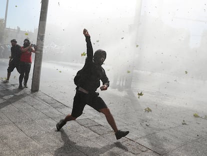 Un manifestante se prepara para lanzar una piedra mientras un coche de la policía antidisturbios lanza un chorro de agua durante  protesta estudiantil en Santiago este 25 de marzo.