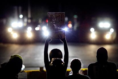 Un manifestante sostiene un cartel con el lema "Justicia y paz", durante una protesta contra la violencia policial y la desigualdad racial, frente a una oficina de policía en Portland (EE UU).