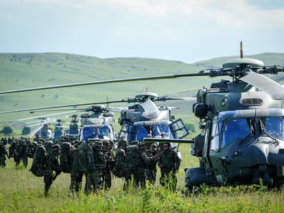 Paratroopers from the German Armed Forces and other NATO partners stand next to German Army NH-90 helicopters during military exercises.