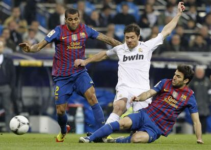 Los azulgrana Dani Alves y Cesc F&agrave;bregas disputan un bal&oacute;n con el jugador del Real Madrid, Xabi Alonso.  