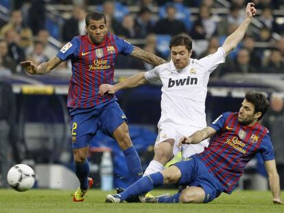 Los azulgrana Dani Alves y Cesc F&agrave;bregas disputan un bal&oacute;n con el jugador del Real Madrid, Xabi Alonso.  