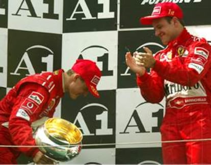 Schumacher se inclina, con el trofeo en la mano, ante Barrichello, que aplaude desde lo alto del podio.