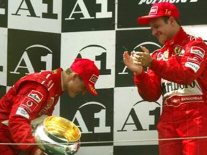 Schumacher se inclina, con el trofeo en la mano, ante Barrichello, que aplaude desde lo alto del podio.