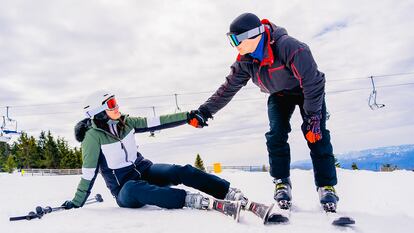 Una persona ayudando a levantarse a otra esquiando en la nieve.