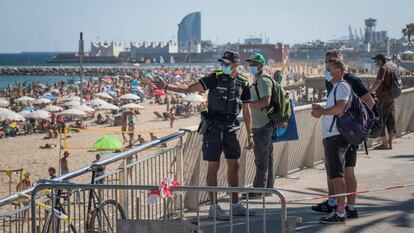 Un policia municipal explica a uns vianants la situació de la platja del Bogatell a Barcelona, diumenge.