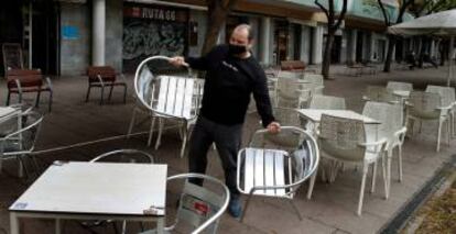 Un camarero prepara la terraza del restaurante donde trabaja para atender a sus clientes.