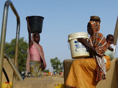 Una niña y una mujer con el hijo a la espalda cargan cubos de agua de hasta 20 litros en el distrito de Sona, Níger. El agotamiento por la sobrecarga de trabajo es una de las razones por las que se complican los embarazos en el país.