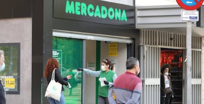 Una trabajadora de un supermercado da guantes a las decenas de personas que esperan una larga cola, en Madrid.