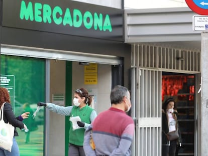 Una trabajadora de un supermercado da guantes a las decenas de personas que esperan una larga cola, en Madrid. 