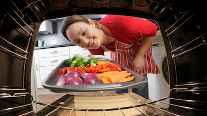 Un mujer metiendo en el horno la bandeja con verduras.
