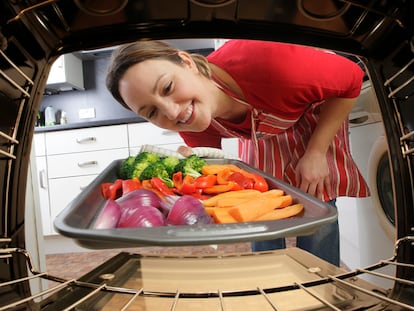 Un mujer metiendo en el horno la bandeja con verduras.