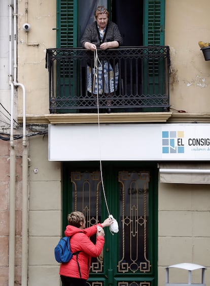 Una mujer facilita comida a una persona mayor gracias a una bolsa colgada de una cuerda desde su balcón.