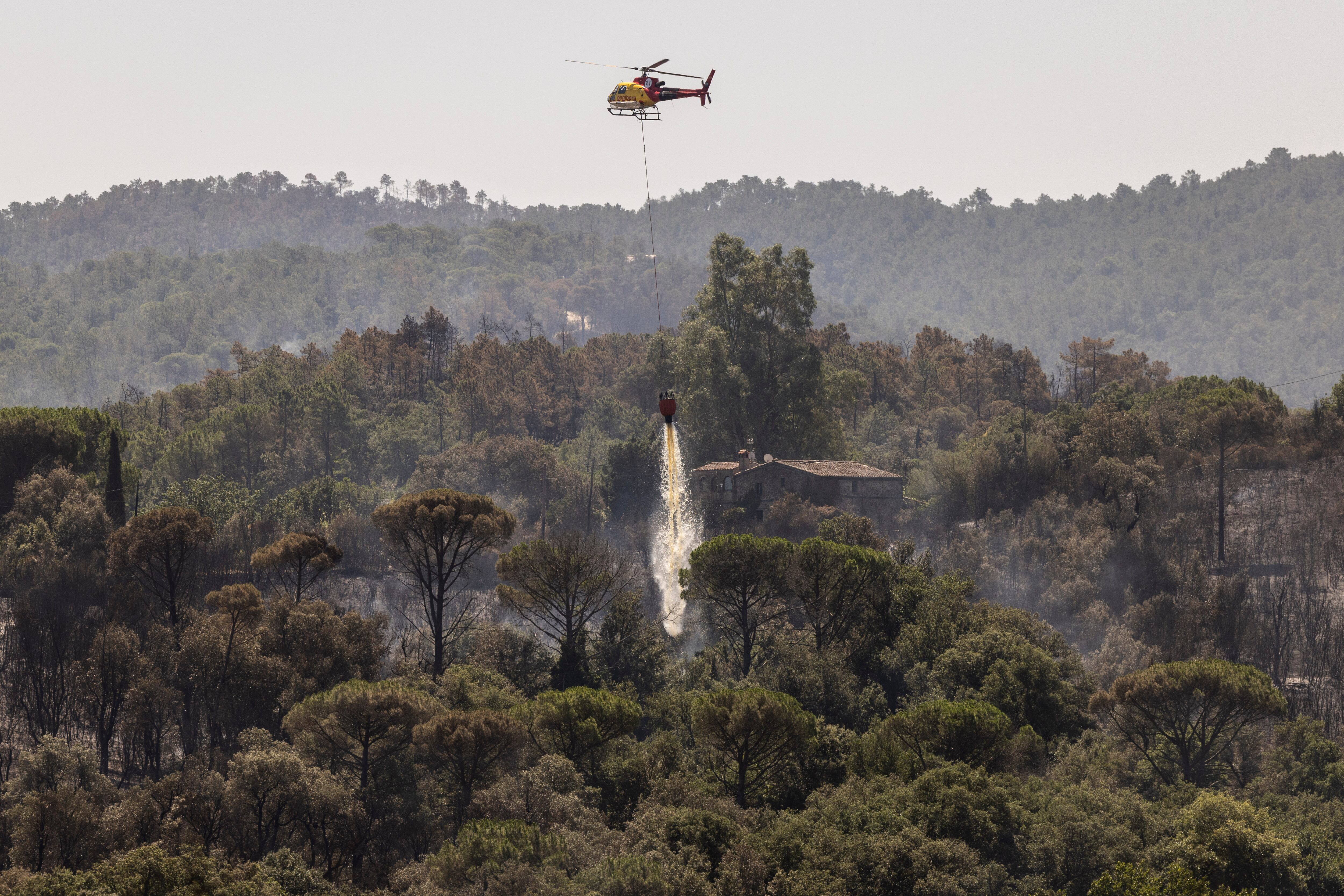 Uno de los cuatro helicópteros que el domingo estuvieron remojando el flanco derecho del incencio de Les Gavarres, en Girona. En la imagen remojando para proteger una masía.