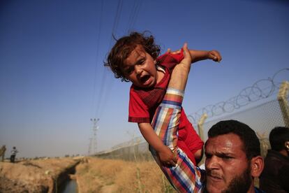 Un refugiado sirio lleva un bebé en alto después de cruzar la valla fronteriza.