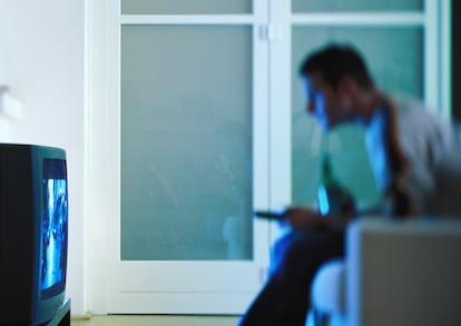 Un hombre, sentado frente al televisor en el salón de su casa.