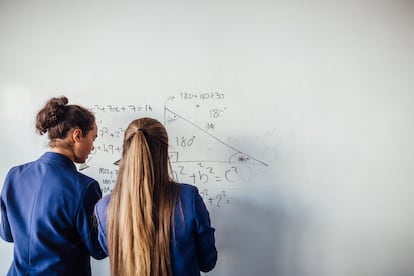 Büyük bir beyaz tahtanın önünde duran iki genç, tahtadaki bir matematik denklemini çözüyor.
