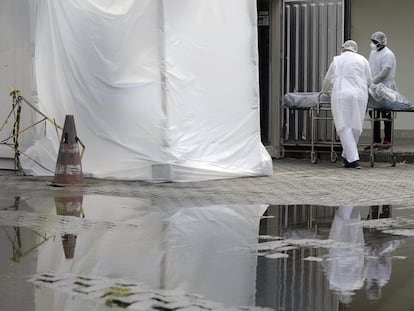 Profissionais de saúde vestindo equipamentos de proteção transportam o corpo de uma pessoa no Rio de Janeiro, em maio.